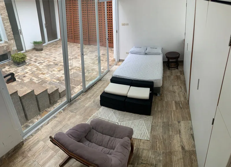 Chambre dont un mur entièrement vitré donne sur le patio intérieur dallé