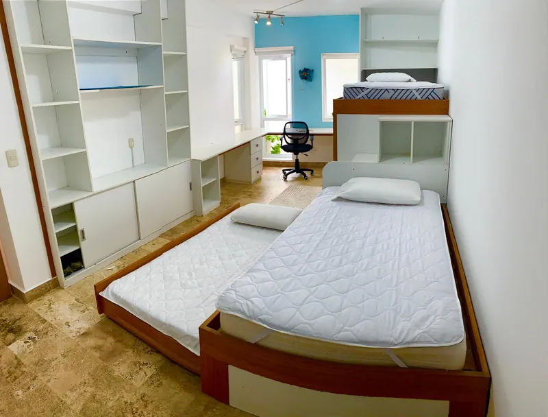 Chambre avec lits simples, étagères et placards intégrés, bureau devant la fenêtre
