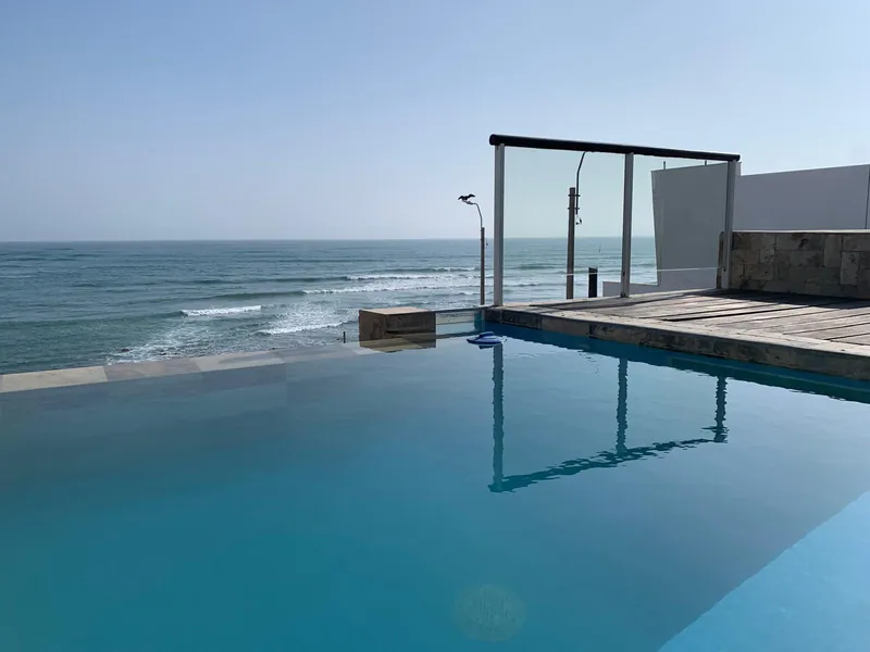 Piscine au bord de la terrasse, dont l'eau semble se prolonger vers l'océan Pacifique, avec garde-corps en verre et deck en bois