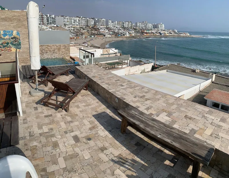Terrasse ensoleillée avec chaises longues et banc en bois, dominant une plage et une baie bordée d'immeubles