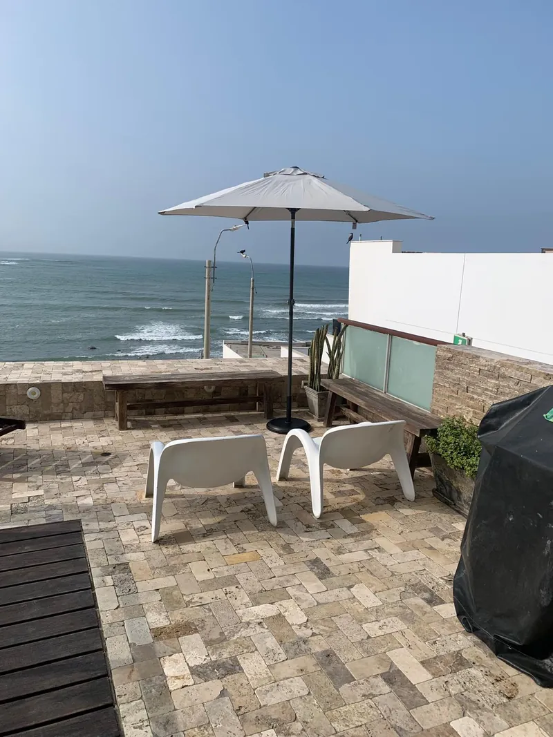 Deux fauteuils blancs, des bancs en bois et un parasol sur la terrasse, face à l'océan